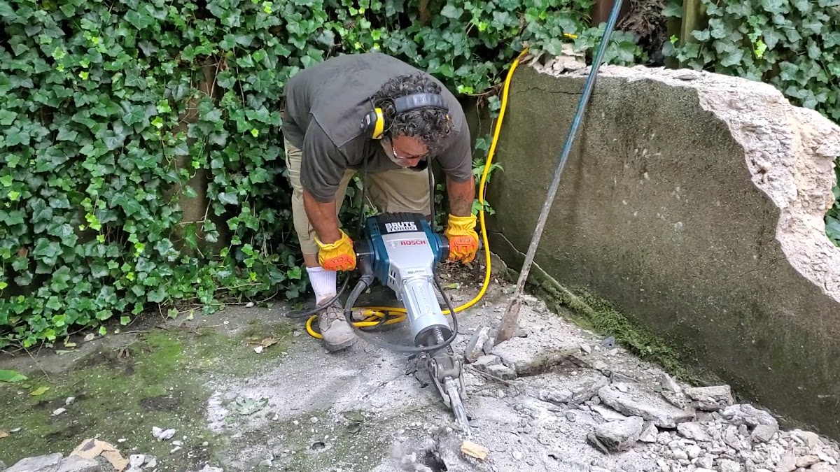 A crew member using a jackhammer to break up a concrete slab
