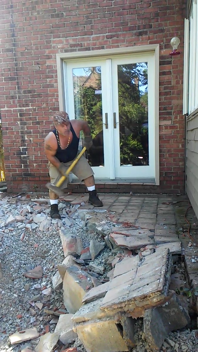 Owner Shorty breaking up an old stone patio by hand with a sledgehammer